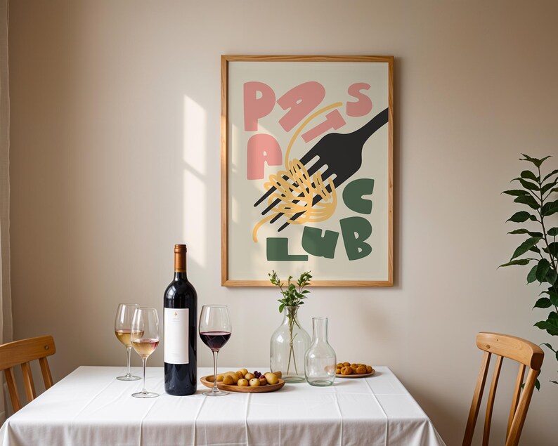 May include: A dining scene with a framed poster that reads "Pasta Club" in pink, black, and green. A bottle of red wine, wine glasses, and a wooden plate of food sit on a white tablecloth. A wooden chair is on either side of the table.