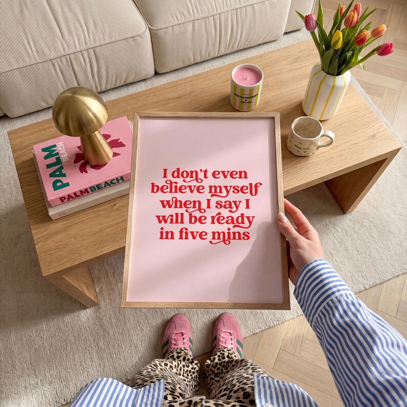 K&ouml;nnte beinhalten: Ein rechteckiges gerahmtes Wandbild mit hellrosa Hintergrund und rotem Text, der lautet: I don't even believe myself when I say I will be ready in five mins. Der Rahmen besteht aus hellem Holz und hat ein schlichtes, klares Design.