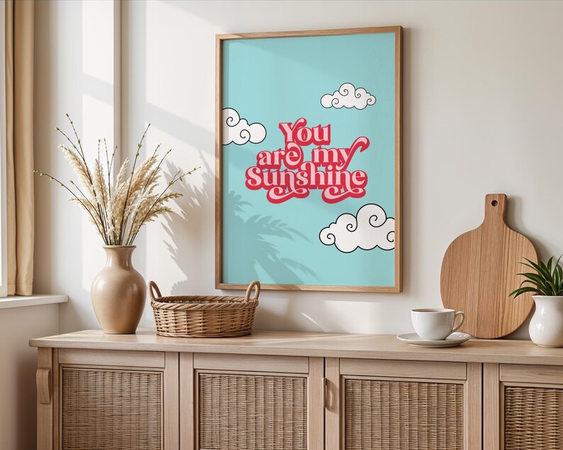 May include: A light blue poster with a white frame. The poster has a pink and white text that says "You are my Sunshine" with white clouds and a palm tree shadow.