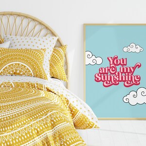 May include: A framed print with a blue background and white clouds. The text "You are my Sunshine" is written in pink with a retro font.