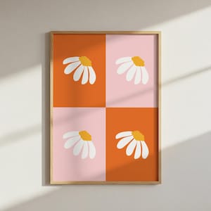 May include: A framed art print featuring a daisy design. The artwork is divided into four quadrants of orange and pink, each with a white daisy with a yellow center. The frame is a light wood color.