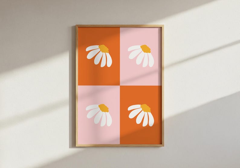 May include: A framed art print featuring a daisy design. The artwork is divided into four quadrants of orange and pink, each with a white daisy with a yellow center. The frame is a light wood color.