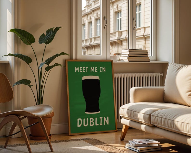 May include: A framed green poster with the text "MEET ME IN DUBLIN" and a graphic of a pint of stout. The poster is in a living room with a beige sofa, wooden chair, and a large potted plant. A window with a view of a building is in the background.