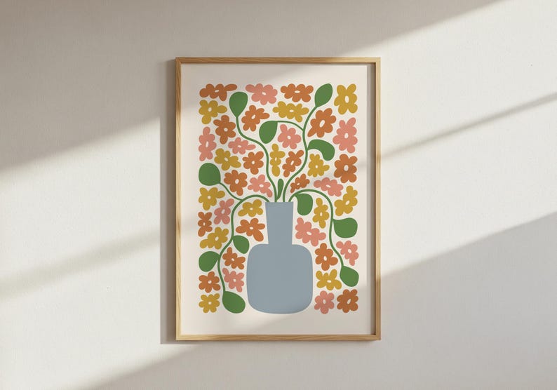 May include: A framed art print featuring a stylized floral arrangement. A light blue vase holds stems with green leaves and orange, pink, and yellow flowers. The artwork is set against a cream background and framed in a light wood.