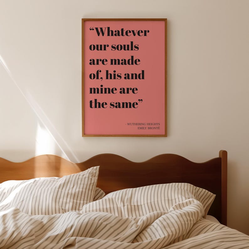 Op de afbeelding: Een rechthoekige wandkunstprint in een houten lijst met een roze achtergrond en zwarte tekst die luidt: Whatever our souls are made of, his and mine are the same. Onder het citaat staat Wuthering Heights door Emily Bronte.