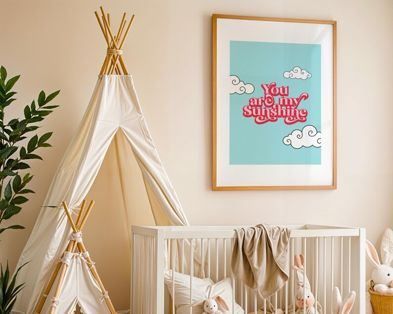 May include: A white teepee tent with a wooden frame, a white crib with a beige blanket, and a framed print with a blue background and the text "You are my sunshine" in pink and white.