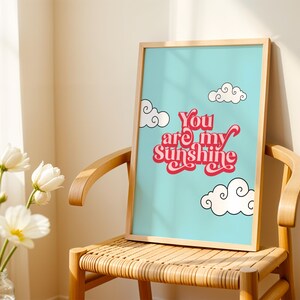 May include: A framed print with a blue background and white clouds. The print features the text "You are my sunshine" in red and pink lettering.