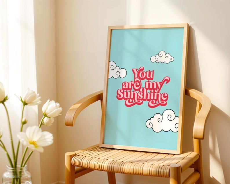 May include: A framed print with a blue background and white clouds. The print features the text "You are my sunshine" in red and pink lettering.