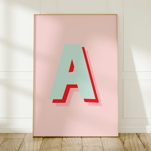 以下が含まれることがあります： 淡いピンクの背景に、中央に大きな大文字の「A」が配置された長方形のウォールアートプリント。文字は淡いミントグリーンで、大胆でオフセットされた赤いドロップシャドウが施されており、立体的な視覚効果を生み出しています。
