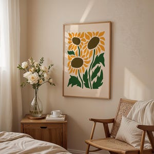 May include: A framed art print featuring a stylized illustration of sunflowers in yellow, green, and brown. The artwork hangs on a beige wall above a wooden chair and a nightstand with a vase of flowers.