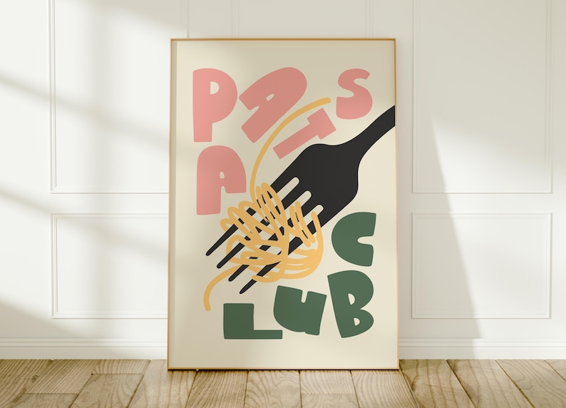 May include: A framed poster with the words "Pasta Club" in pink and green block letters. A black fork is intertwined with yellow spaghetti. The poster is displayed on a wooden floor against a white wall.