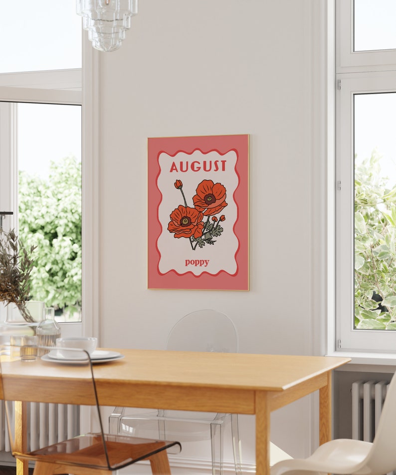 May include: A framed art print featuring a stylized illustration of red poppies. The word "AUGUST" is at the top, and "poppy" is at the bottom. The artwork has a pink border and a gold frame, suitable for wall decor.