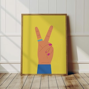 May include: A framed art print featuring a hand making the peace sign against a yellow background. The hand is tan with pink fingernails and a blue and yellow ring. The sleeve is blue.