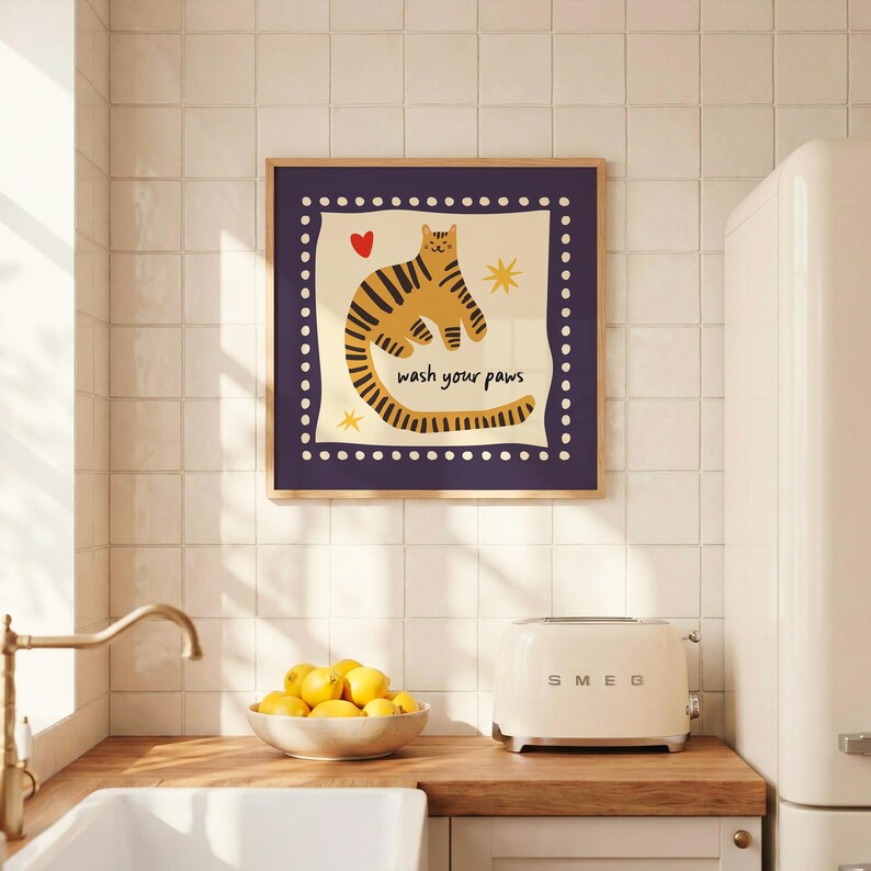 K&ouml;nnte beinhalten: Ein quadratischer Wandkunstdruck in einem Holzrahmen mit einer stilisierten orangefarbenen getigerten Katze mit schwarzen Streifen auf cremefarbenem Hintergrund. Der Text "wash your paws" ist schwarz geschrieben, erg&auml;nzt durch ein kleines rotes Herz und zwei gelbe Sterne.