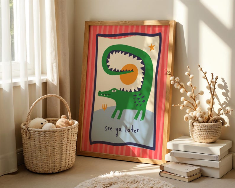 Pu&ograve; includere: Una stampa artistica rettangolare incorniciata raffigurante un coccodrillo verde con la coda curva, un sole giallo e una piccola stella arancione. L'illustrazione include il testo "see ya later" in blu scuro su un bordo a righe rosse e rosa.