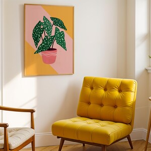 May include: A framed art print of a potted plant with green, speckled leaves. The artwork hangs above a yellow tufted armchair. A second chair with a wooden frame and a cream cushion is also visible.