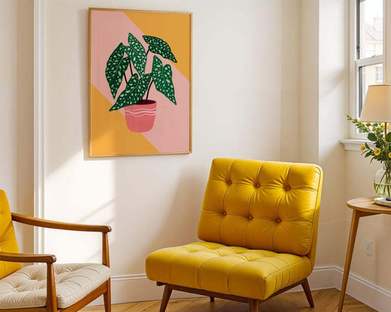 May include: A framed art print of a potted plant with green, speckled leaves. The artwork hangs above a yellow tufted armchair. A second chair with a wooden frame and a cream cushion is also visible.