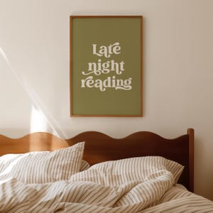 May include: A framed print with the words "Late night reading" in white script on an olive green background. The print is hanging above a bed with striped bedding and a wooden headboard.