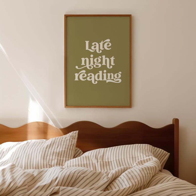 May include: A framed print with the words "Late night reading" in white script on an olive green background. The print is hanging above a bed with striped bedding and a wooden headboard.