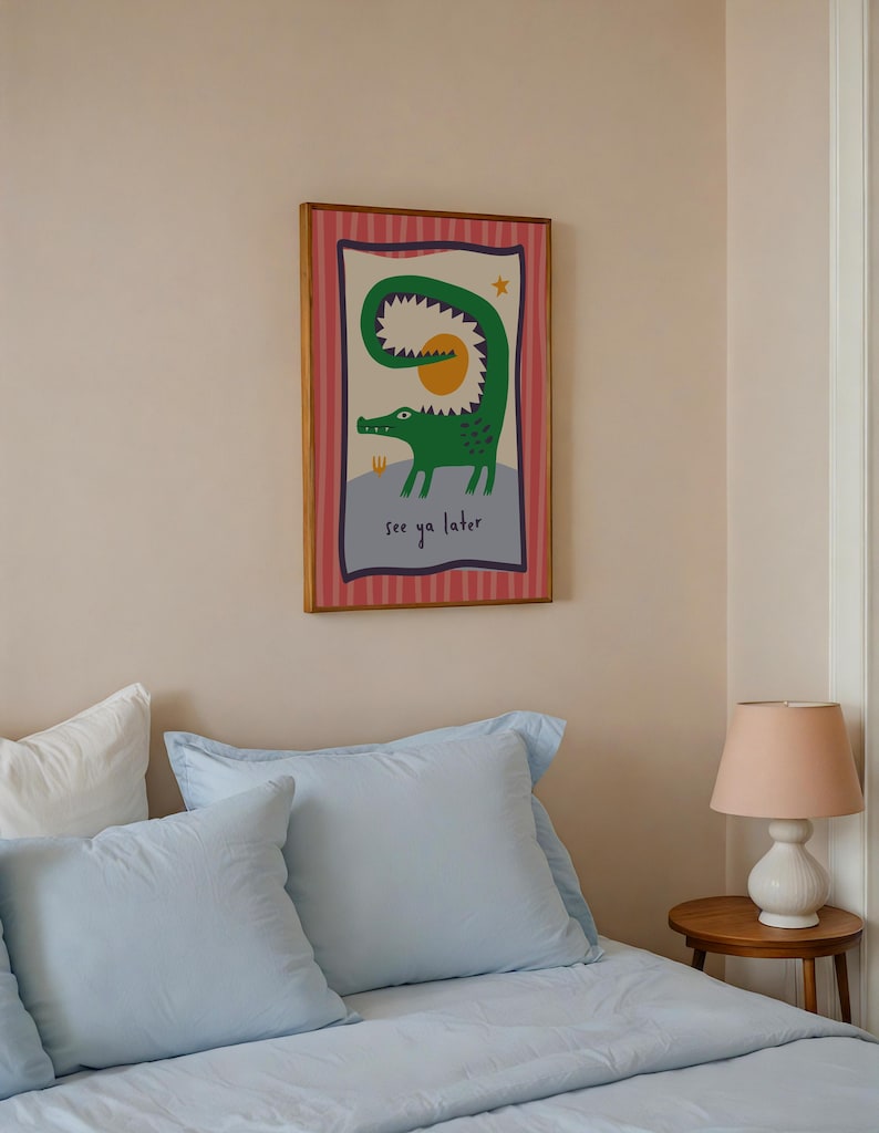 Pu&ograve; includere: Una stampa artistica da parete rettangolare incorniciata raffigurante un coccodrillo verde con la coda curva, un sole giallo e una piccola stella su sfondo chiaro. Il bordo &egrave; rosa a righe verticali e il testo see ya later &egrave; in basso.