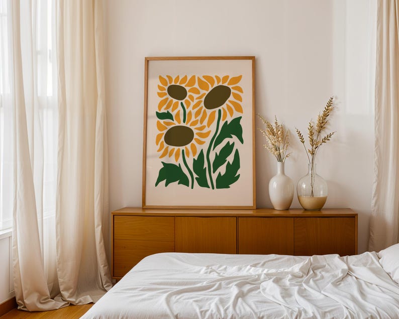 May include: A framed art print featuring a stylized illustration of three sunflowers in shades of yellow, brown, and green. The artwork is displayed above a wooden cabinet, with vases of dried plants. The room has a neutral color palette.