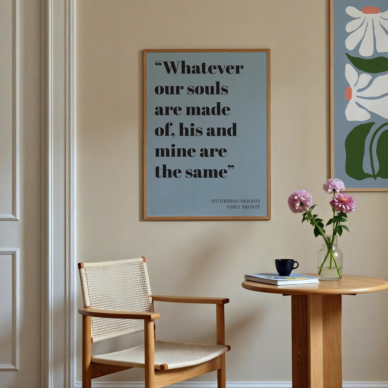 Op de afbeelding: Een rechthoekige wandkunstprint in een houten lijst met het citaat "Whatever our souls are made of, his and mine are the same" in een zwart schreeflettertype op een stoffige blauwe achtergrond, met de tekst "Wuthering Heights Emily Bronte" eronder.