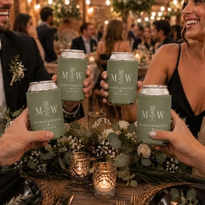 May include: Four sage green foam can coolers held in a toast. Each cooler features white text with the initials M W, the names Mauricio & Whitney, and the date 10.12.2030, accented by a small heart and a vertical leafy branch illustration.