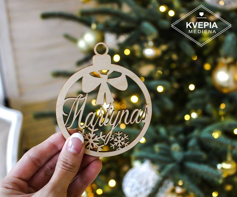May include: A wooden Christmas ornament shaped like a ball with the name "Martynas" cut out. The ornament has a bow and snowflakes cut out around the name.