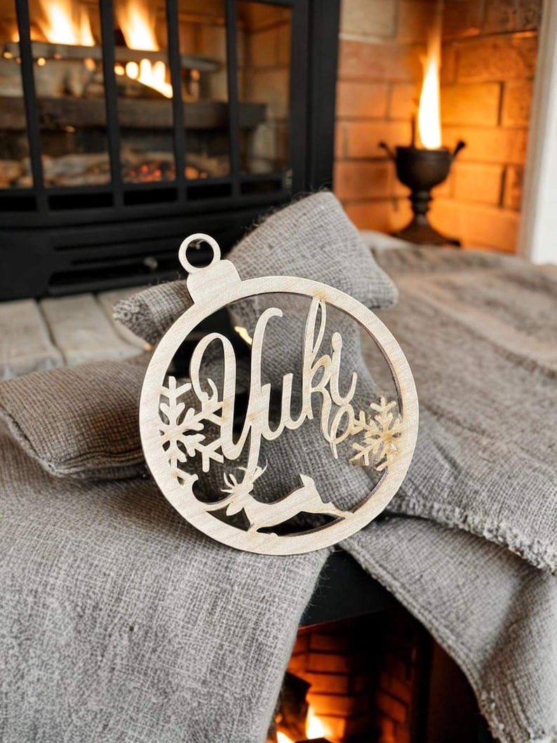 May include: A wooden Christmas ornament with a reindeer and snowflake design. The ornament is personalized with the name "Yuki".