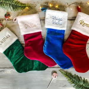 May include: Four personalized Christmas stockings with white fur trim. The stockings are green, red, blue, and pink. The names on the stockings are Matthias, Mia, Hugo Hans, and Remo.