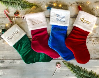 May include: Four personalized Christmas stockings with white fur trim. The stockings are green, red, blue, and pink. The names on the stockings are Matthias, Mia, Hugo Hans, and Remo.