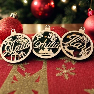 May include: Three wooden Christmas ornaments with names "Jalto", "Emilia", and "Mari" written on them. The ornaments are decorated with snowflakes and other festive designs.