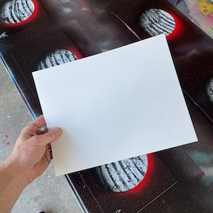 May include: A white sheet of paper is held over a black and red background with white and gray circles. The circles have a red outline and are painted with white stripes.