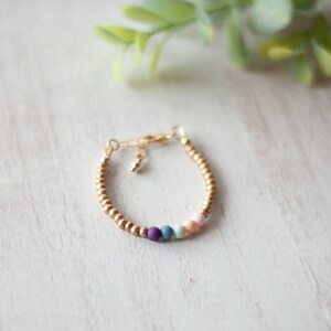 May include: A gold beaded bracelet with a clasp closure and five colorful beads in shades of purple, blue, green, and pink.