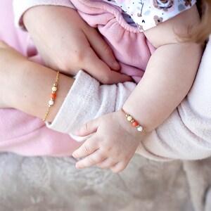 May include: Two gold bracelets with colorful beads. The bracelets are on the wrists of a baby and an adult.