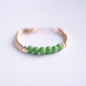 May include: A gold ring with a row of five green beads.
