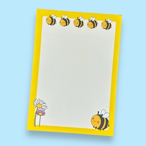 May include: A yellow notepad with a white interior and a yellow border. The border is decorated with cartoon bees and a single daisy. The notepad has a bee design at the bottom.