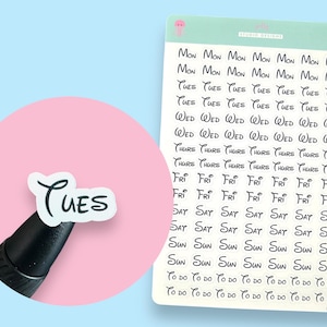 May include: A sheet of white stickers with black text. The stickers feature the days of the week written in a Disney-inspired font. The word "Tues" is highlighted on a separate sticker.