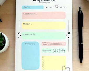 May include: A white notepad with the text "Today's Game Plan" and sections for date, priorities, and mood tracking. A black pen rests on the right. The notepad has pastel-colored boxes and heart-shaped icons.