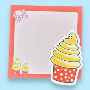May include: A pink and white polka dot bow sits on a red and white polka dot notepad with a yellow and white swirl cupcake illustration.