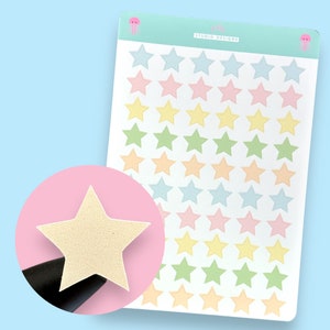 May include: A sheet of pastel coloured star stickers. The sheet has 36 stars in total, with 9 stars in each of the four colours: light blue, pink, yellow, and green. The stars are outlined in a darker shade of the same colour. The sheet has the text "jelly" and "STUDIO DESIGNS" printed at the top.