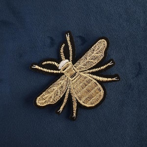 May include: A gold embroidered bee patch on a dark blue fabric background.