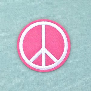 Op de afbeelding: Een ronde geborduurde patch met een felroze achtergrond en een wit vredesteken in het midden van het ontwerp. De patch heeft een strakke witte rand die de cirkelvorm omlijnt en een duidelijk contrast vormt met de roze kleur.