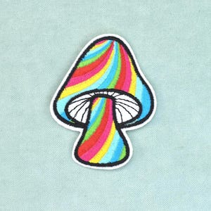 Può includere: Una toppa ricamata a forma di fungo con un vivace motivo a spirale color arcobaleno sul cappello e sul gambo. La parte inferiore del cappello è bianca con lamelle nere ricamate e l'intero disegno è rifinito con un contorno nero.