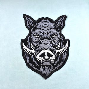 Peut inclure: Un écusson brodé noir et gris représentant une illustration détaillée d'une tête de sanglier. Le motif comprend des défenses proéminentes et une expression sévère, adapté aux vestes, sacs ou autres vêtements.