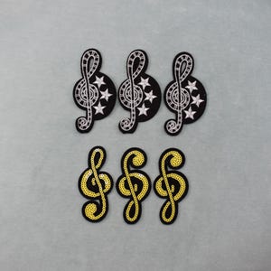 Peut inclure: Six écussons en forme de notes de musique. Trois sont noirs avec des motifs de clé de sol et d'étoiles blanches. Les trois autres sont noirs avec des motifs de clé de sol à paillettes jaunes. Idéal pour les vêtements.
