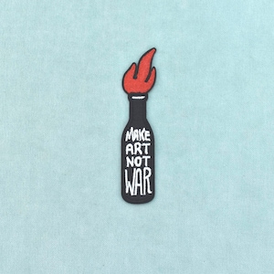 Könnte beinhalten: Ein gestickter Aufnäher in Form einer Flasche mit einer roten Flamme an der Spitze. Die Flasche ist schwarz und trägt den weißen Schriftzug "MAKE ART NOT WAR" in einer stilisierten Schriftart. Das Design hat klare Konturen und feine Stickereien.