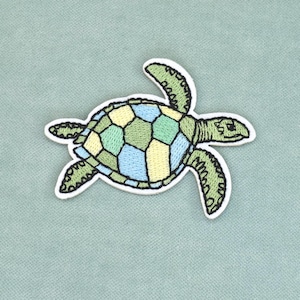Peut inclure: Un écusson brodé thermocollant en forme de tortue de mer. La tortue présente une carapace avec un motif géométrique dans des tons vert clair, jaune pâle et bleu ciel, avec des contours vert foncé et une tête et des nageoires vert uni.
