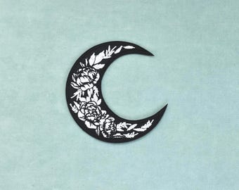 May include: A crescent moon shaped patch featuring a black background with a white embroidered floral design. The floral pattern consists of detailed peony-like flowers and leaves arranged along the curve of the moon shape with clean edges.