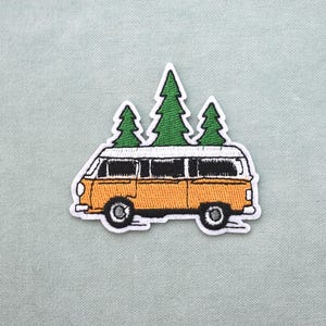 May include: Embroidered patch showing a yellow vintage van with a white roof and three green pine trees. The patch has a white border on a light green background. Suitable for application on clothing or accessories. The van is approximately 10 cm long.